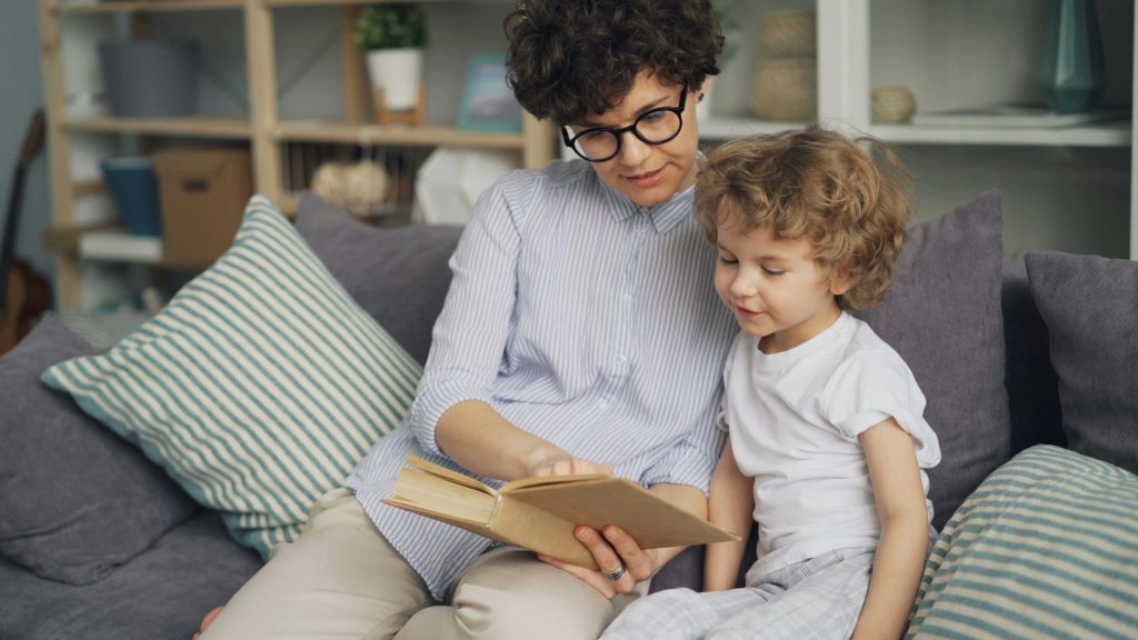 A mother reads a book to her young son on a cozy couch, fostering bonding and education.