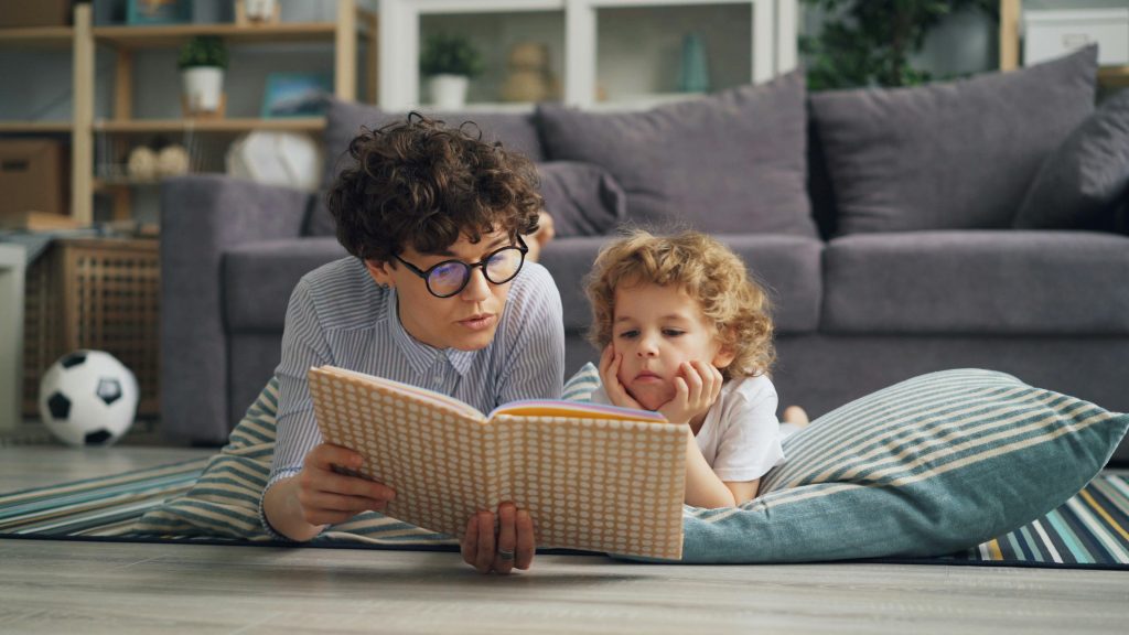 A mother and young child reading a book on the living room floor, fostering love for reading.