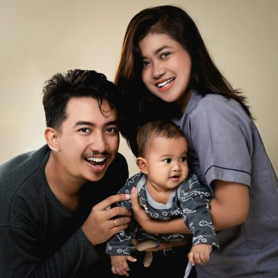 A joyful family portrait featuring smiling parents and their adorable baby in a warm setting.